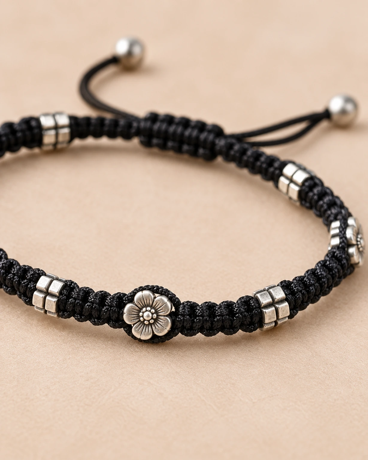 Close-up of oxidised silver flower charm and spacer beads on black macramé thread.