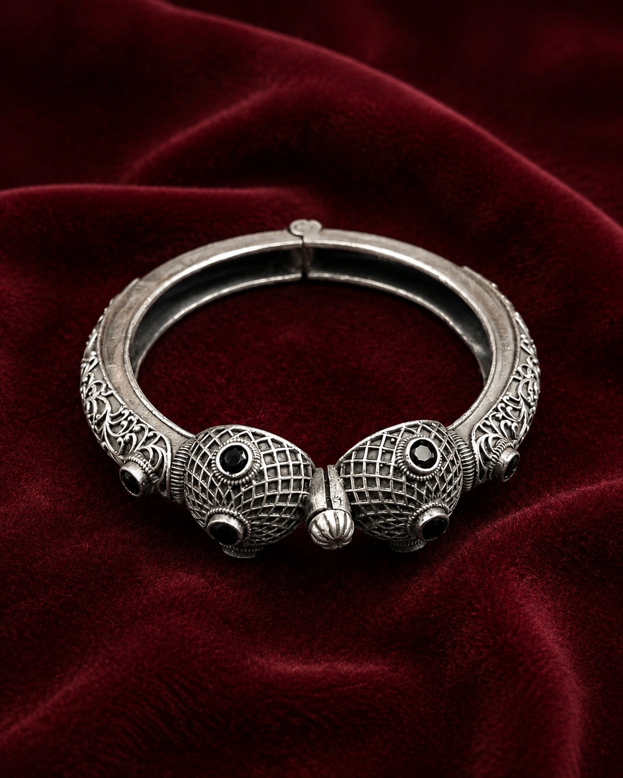 Designer silver kada bracelet displayed on rich burgundy velvet.