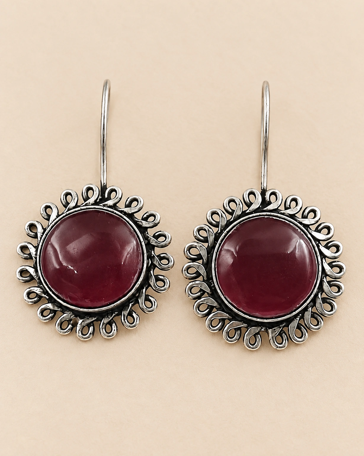 Maroon floral round hook earrings shown in a detailed close-up on pale beige.
