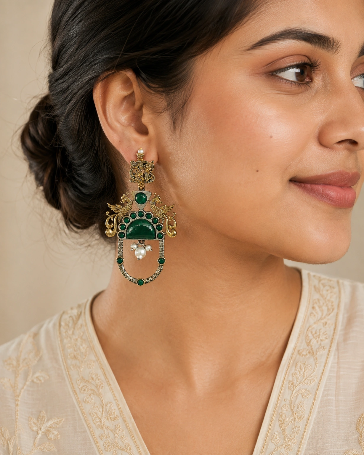 Green two-tone peacock earrings worn naturally with an ivory outfit.