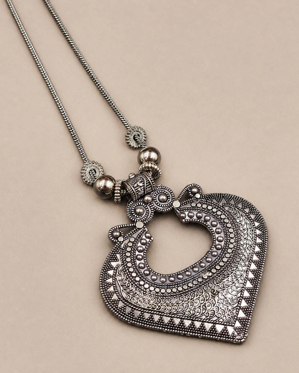 Oxidized silver necklace shown in a detailed close-up on pale beige.