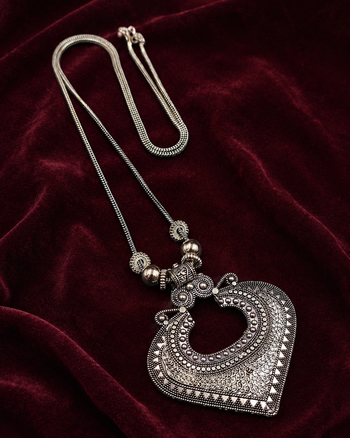 Oxidized silver necklace displayed on rich burgundy velvet.