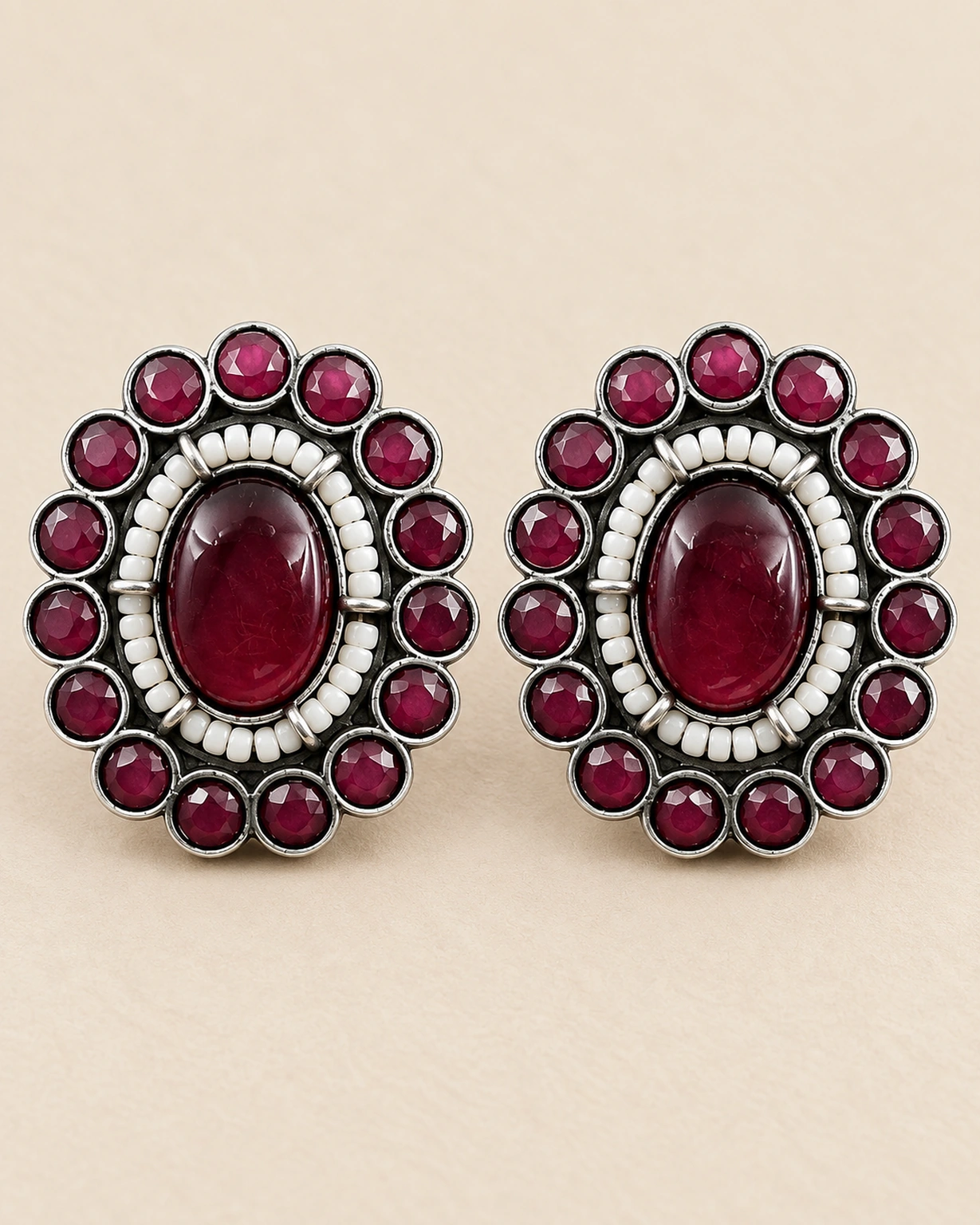 Maroon round stud earrings shown in a detailed close-up on pale beige.