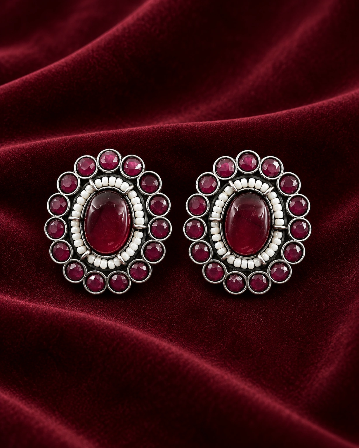 Maroon round stud earrings displayed on rich burgundy velvet.