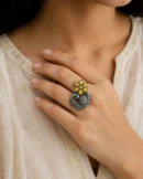 Yellow flower peacock ring with a green eye worn on a woman's hand.