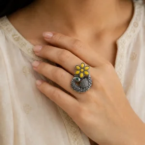 Yellow flower peacock ring with a green eye worn on a woman's hand.