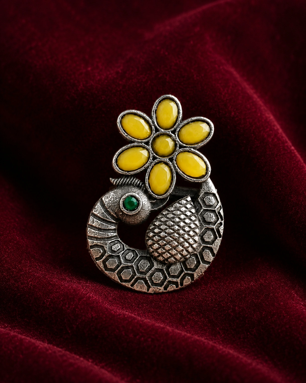 Yellow-green peacock ring resting on burgundy velvet, showing its curled silver-tone body.